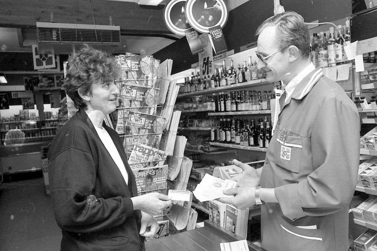 Sjælland 1985: Den venlige købmand låner penge ud. Fattigfirserne var en hård tid i mange danske husholdninger. Lille købmand i Nødebo nær Hillerød udlåner penge til en af sine trofaste, men trængende kunder. (Foto: Lokalarkivet Alsønderup-Tjæreby)